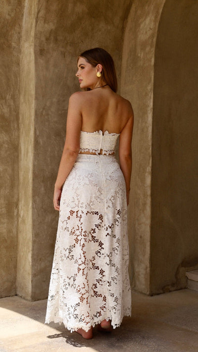 Woman in a white lace dress standing against a textured wall.